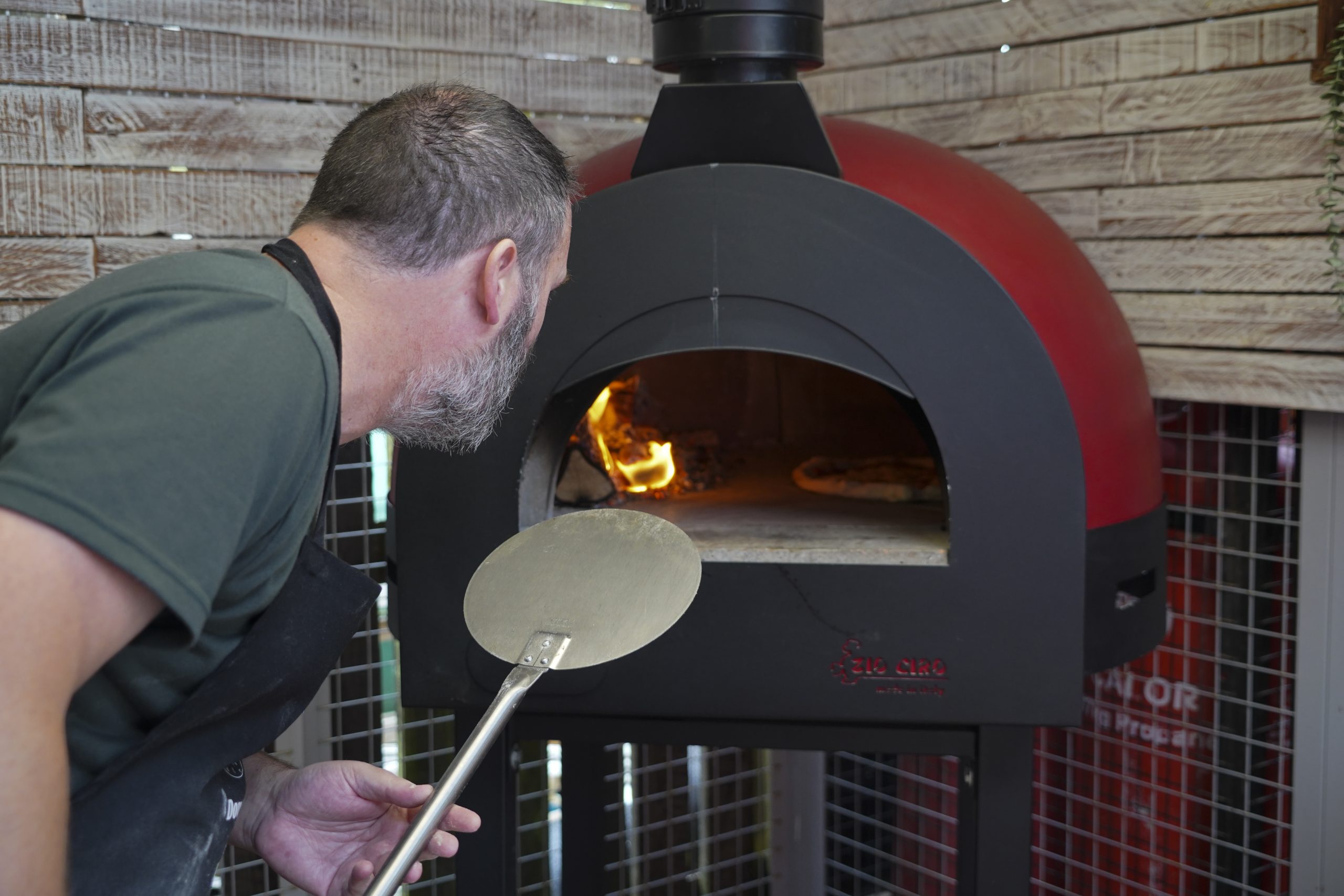 Image from White's Pizza School- man using Zio Ciro oven to cook his pizza holding a Gi Metal Turning Peel.